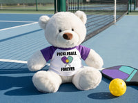 Pickleball Teddy Bear - Personalized 10" Creamy White Nuzzles Bear, Paddle Design - purple sleeves, pictured on pickleball court. Perfect gift for pickleball players.